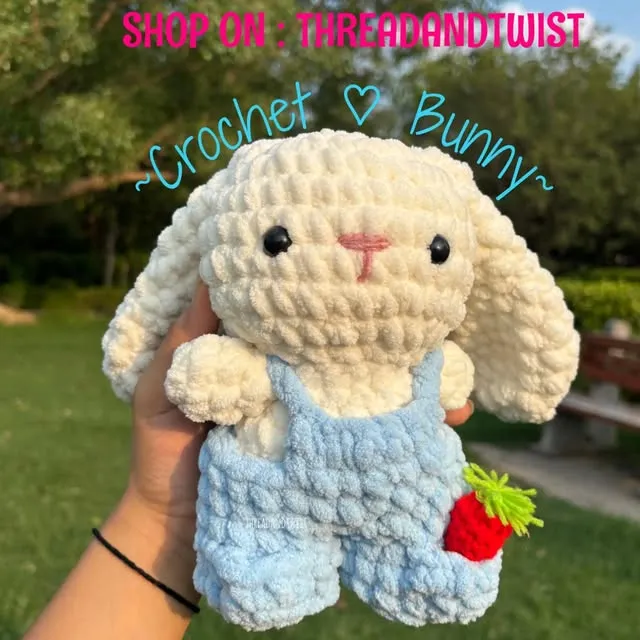 Cream crochet bunny wearing blue dungarees, held outdoors