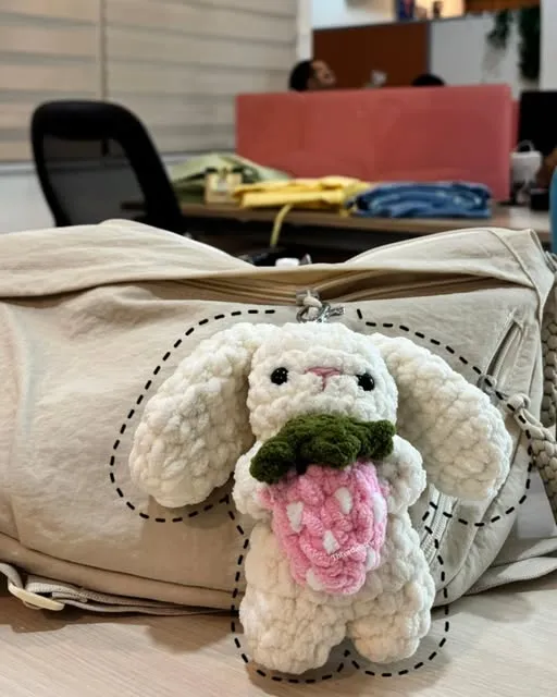 Bunny bag charm holding a pink bouquet, clipped to a bag
